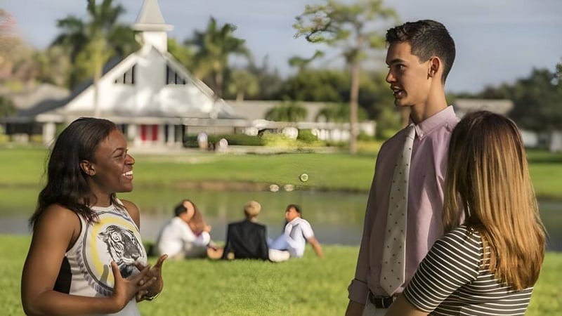 Zwei Schüler der Saint Andrews School unterhalten sich auf einer Wiese mit einer Kirchenähnlichen Struktur im Hintergrund.
