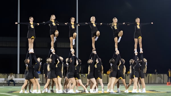 Eine Gruppe von Cheerleaderinnen führt eine synchronisierte Routine auf dem Sportfeld der Saint Anthony's High School bei Nacht auf.