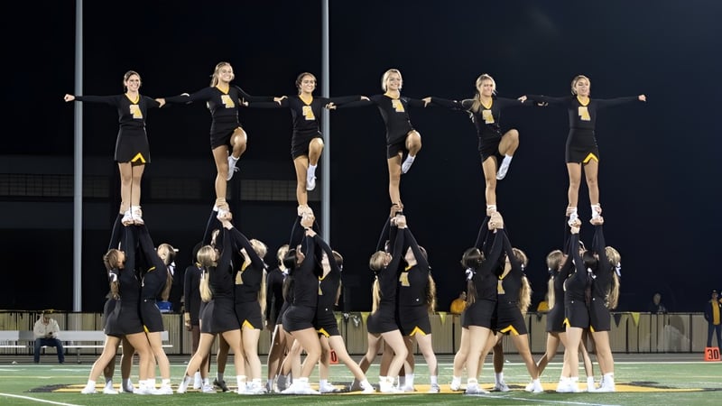 Eine Gruppe von Cheerleaderinnen führt eine synchronisierte Routine auf dem Sportfeld der Saint Anthony's High School bei Nacht auf.