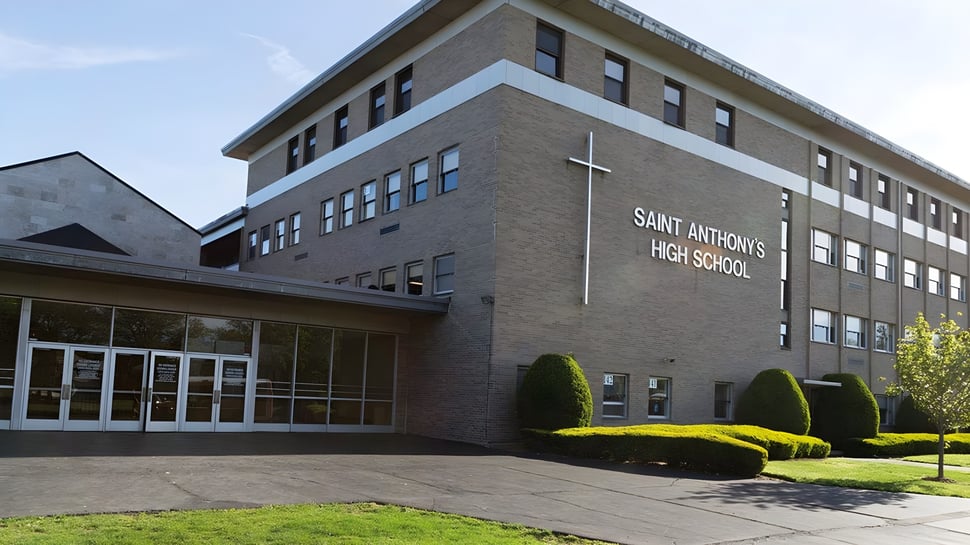 Das Backsteingebäude von Saint Anthony's High School mit einem Kreuz an der Fassade und einer bepflanzten Einfahrt.