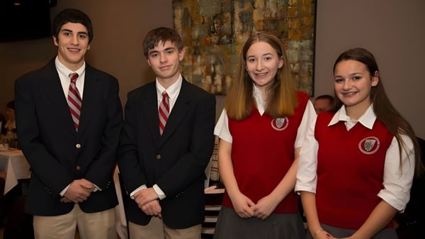 Vier Schüler der Saint Bernard School stehen in formaler Kleidung zusammen in einem schulischen Umfeld.