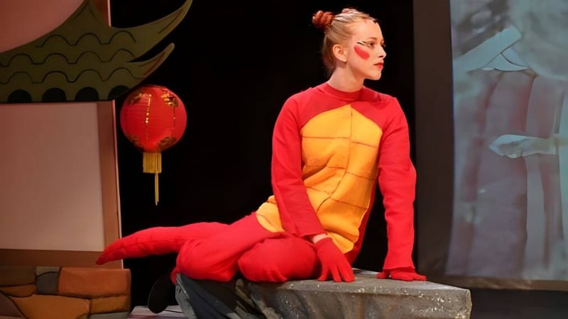 Eine Person in rotem und gelbem Kostüm steht auf der Bühne der Saint Edward's School mit chinesischen Laternen im Hintergrund.