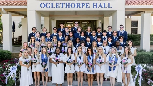 Eine große Gruppe Schülerinnen in weißen Abschlussroben feiert die Graduierung vor dem Oglethorpe Hall auf dem Campus der Saint Edward's School.