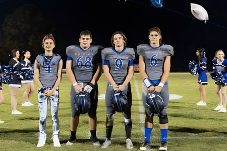 Eine Gruppe Cheerleader der Saint Francis Catholic Academy steht abends auf dem Footballfeld unter heller Beleuchtung.