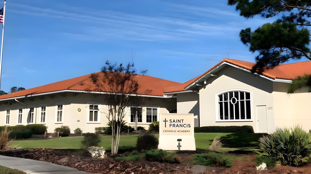 Das Gebäude der Saint Francis Catholic Academy mit rotem Ziegeldach steht in einer gepflegten Anlage mit Bäumen und Sträuchern.