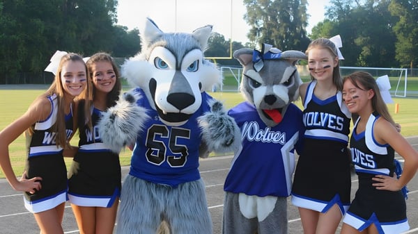 Eine Gruppe Schülerinnen der Saint Francis Catholic Academy posiert auf dem Sportfeld mit dem Maskottchen in Sportuniformen.