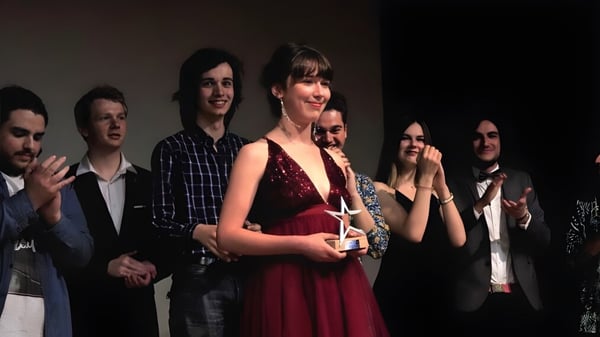 Eine Gruppe von Schülerinnen und Schülern steht auf der Bühne der Saint-Genès La Salle Schule, dabei trägt eine Person ein rotes Kleid.