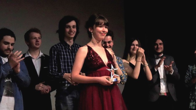 Eine Gruppe von Schülerinnen und Schülern steht gemeinsam auf der Bühne der Saint-Genès La Salle, die zentrale Person trägt ein rotes Kleid.