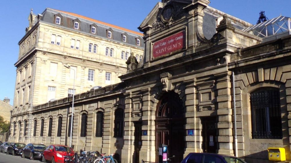 Das geschmückte Hauptgebäude der Saint-Genès La Salle Schule mit einem Parkplatz und einer Straße im Hintergrund.