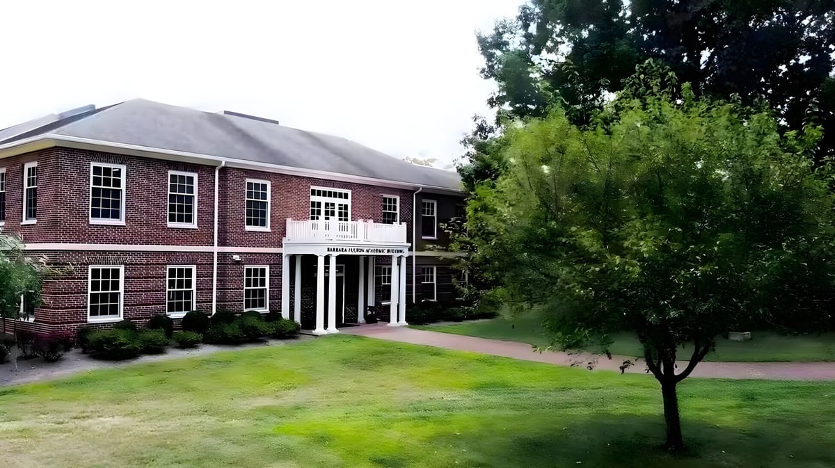 Das Backsteingebäude mit einer Säulenfassade der Saint James School steht in einer grasbewachsenen Fläche mit Bäumen.