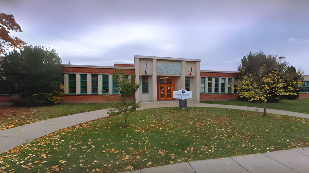 Das moderne Backsteingebäude der Saint-Lambert International High School mit großen Fenstern und herbstlich gestaltetem Rasen.