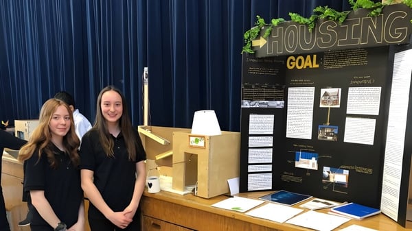 Zwei Schülerinnen der Saint-Lambert International High School stehen vor einem Informationsboard mit dem Titel Housing.