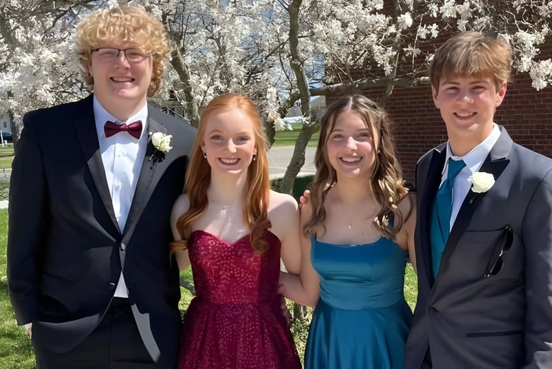 Vier Schülerinnen und Schüler der Saint Paul Lutheran High School stehen in formeller Kleidung zusammen in einem Park mit blühenden Bäumen.