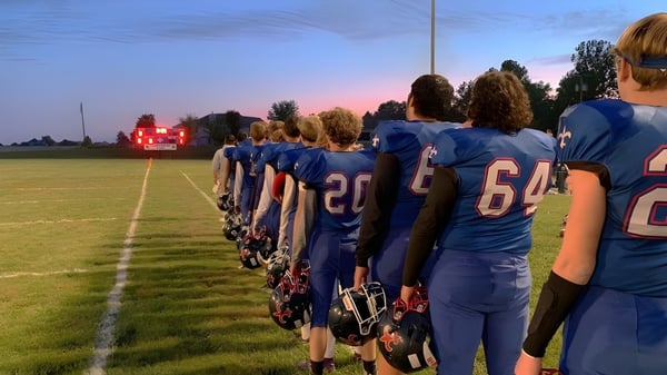 Eine Gruppe von Fußballspielern in blauen Trikots steht auf dem Spielfeld der Saint Paul Lutheran High School bei Sonnenuntergang.