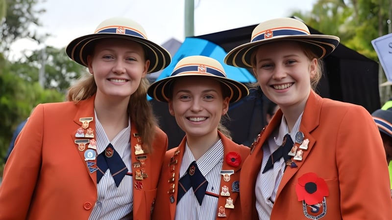 Drei Schülerinnen in orangen Uniformen stehen lächelnd vor Bäumen auf dem Campus des Saint Stephen’s College.