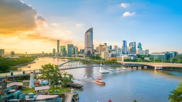 Eine lebhafte Stadtansicht mit modernen Wolkenkratzern und einem belebten Fluss unter einem farbenfrohen Sonnenuntergang, nahe Saint Stephen’s College.