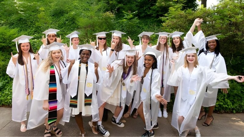 Eine Gruppe Schülerinnen der Salem Academy steht in weißen Abschlussroben im grünen Außenbereich zusammen.