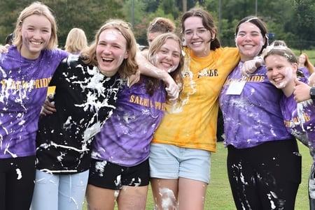 Eine Gruppe von Schülerinnen der Salem Academy umarmt sich draußen vor Bäumen und Grünfläche.