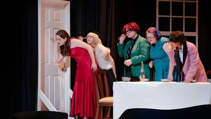 Eine Gruppe von Personen steht in bunten Outfits auf der Bühne der Salem Academy vor einem weißen Tisch.