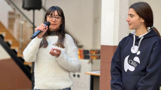 Zwei Schülerinnen der Salesianas führen ein Gespräch in einem Innenraum mit Regalen im Hintergrund.