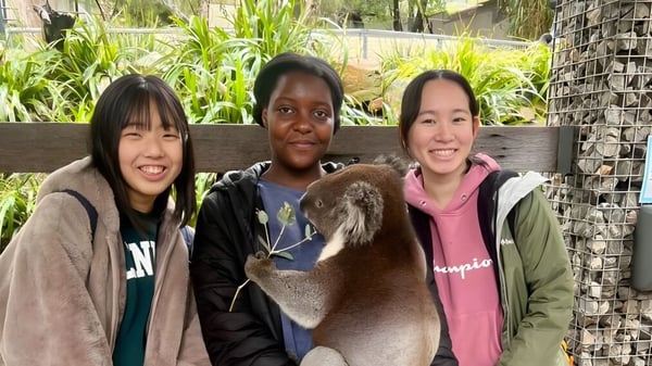 Drei Schüler der Salisbury East High School stehen vor einem grünen Garten und unterhalten sich freundlich.
