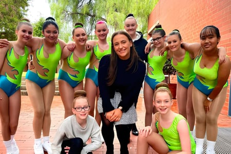 Eine Gruppe Schülerinnen in sportlicher Kleidung steht vor einem Backsteingebäude auf dem Gelände der Salisbury East High School.