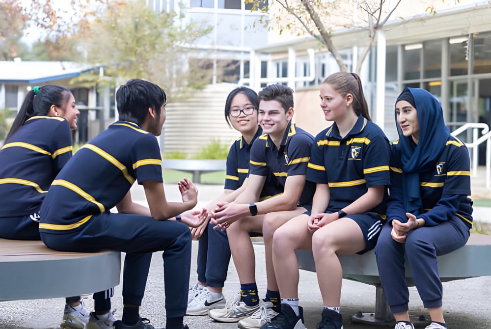 Schüler der Salisbury High School sitzen gemeinsam auf einer Bank im Freien vor Bäumen und Gebäuden.