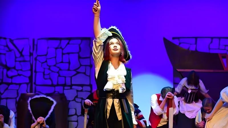 Eine Frau im Kostüm steht mit erhobenen Armen auf der Bühne bei einer Aufführung der Salisbury High School.
