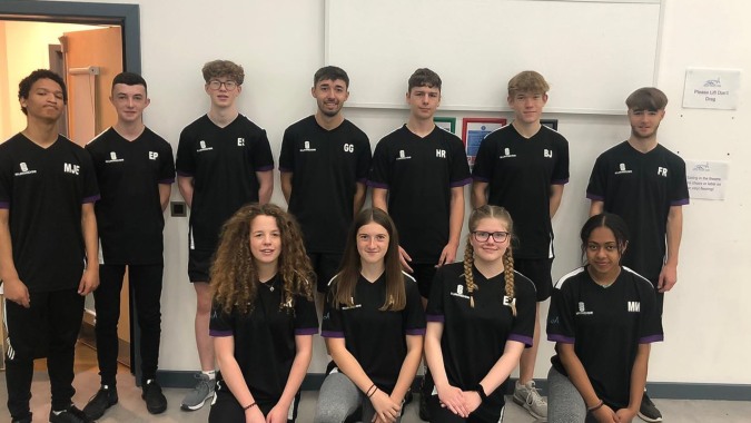Eine Gruppe Schülerinnen und Schüler des Salisbury Sixth Form College steht in einem Schulgebäude und trägt schwarze Shirts mit Logo.