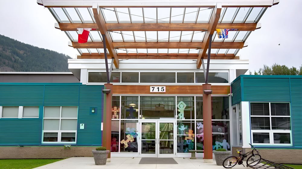 Das moderne mehrstöckige Gebäude der Salmo Secondary School mit Holzrahmen und Glaswänden ist von einer Grünfläche umgeben.