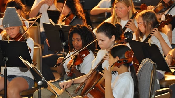 Eine Gruppe von Schülerinnen der Salmo Secondary School spielt verschiedene Streichinstrumente auf der Bühne vor einem Publikum.