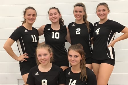 Sechs Schülerinnen der Salmo Secondary School posieren gemeinsam in schwarzen Volleyballuniformen vor einer weißen Wand.