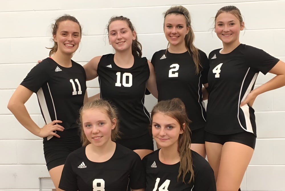 Sechs Schülerinnen der Salmo Secondary School posieren gemeinsam in schwarzen Volleyballuniformen vor einer weißen Wand.