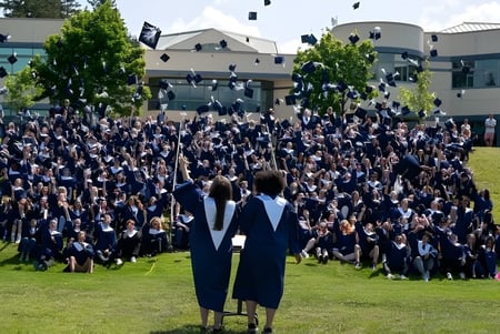 Eine Gruppe Absolventen der Salmon Arm Secondary in schwarzen Talaren steht vor einem Gebäude auf einem Rasenfeld und feiert ihren Abschluss.