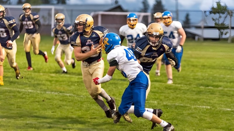 Eine Gruppe Footballspieler der Salmon Arm Secondary spielt intensiv auf dem Rasenfeld mit Zuschauern im Hintergrund.