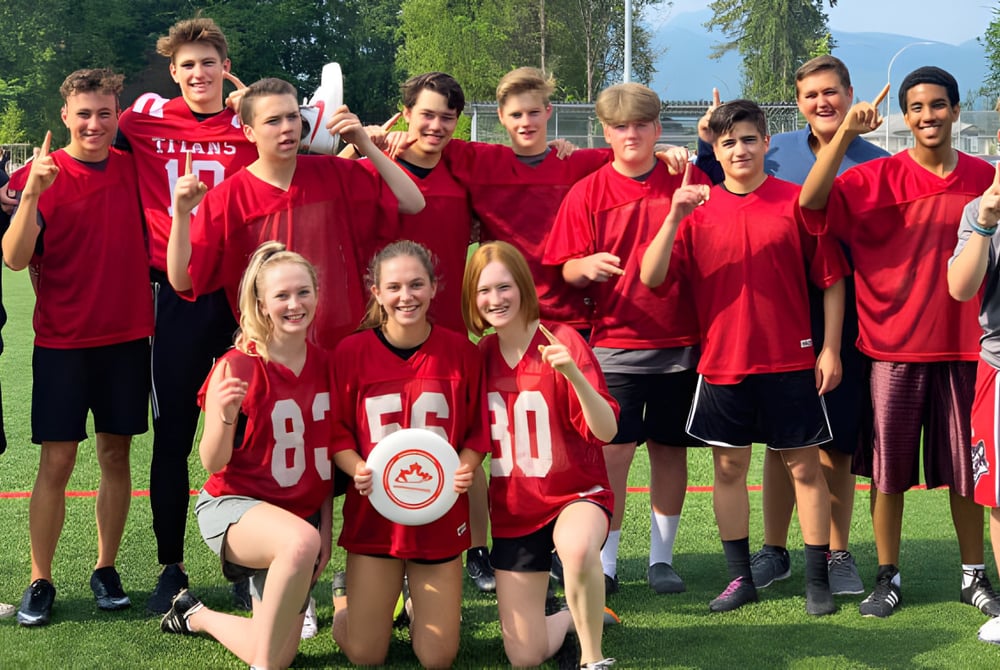 Eine Gruppe von Schülerinnen und Schülern der Samuel Robertson Secondary School steht auf einem Sportfeld mit roter Sportkleidung.