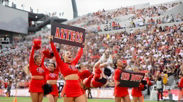 Schülerinnen und Schüler der San Diego State University feuern im Stadion mit roten Uniformen und Cheerleading-Outfits an.