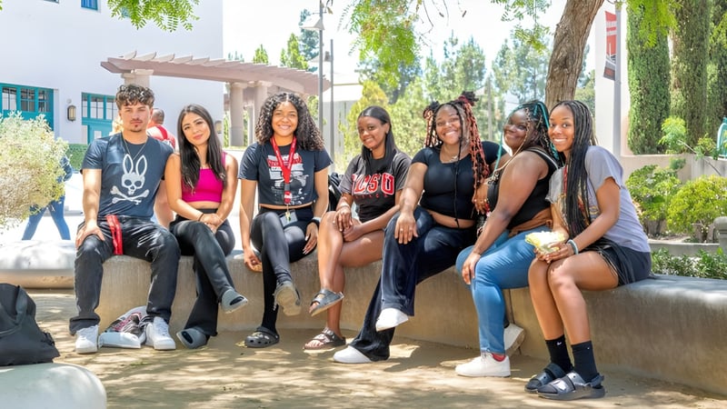Eine Gruppe Schüler sitzt gemeinsam auf einer Bank im Außenbereich auf dem Campus der San Diego State University.