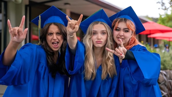Drei Schülerinnen der San Domenico School tragen blaue Abschlussroben und posieren vor einem roten Zelt mit Friedenszeichen.