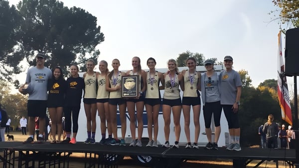 Eine Gruppe junger Athletinnen der San Luis Obispo High School steht mit Pokalen auf einer Bühne vor Bäumen und klarem Himmel.