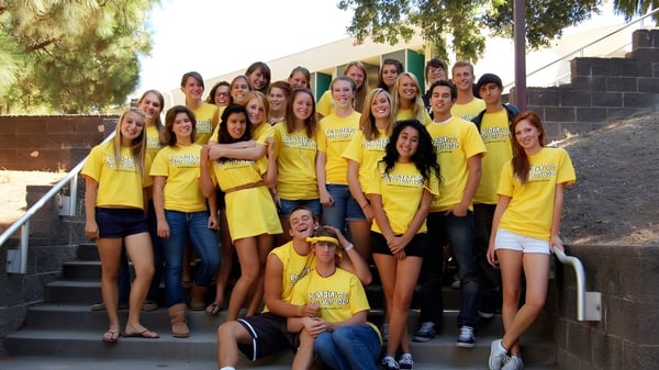 Eine Gruppe Schülerinnen der San Luis Obispo High School sitzt auf Außentreppen vor einem Gebäude und Bäumen.