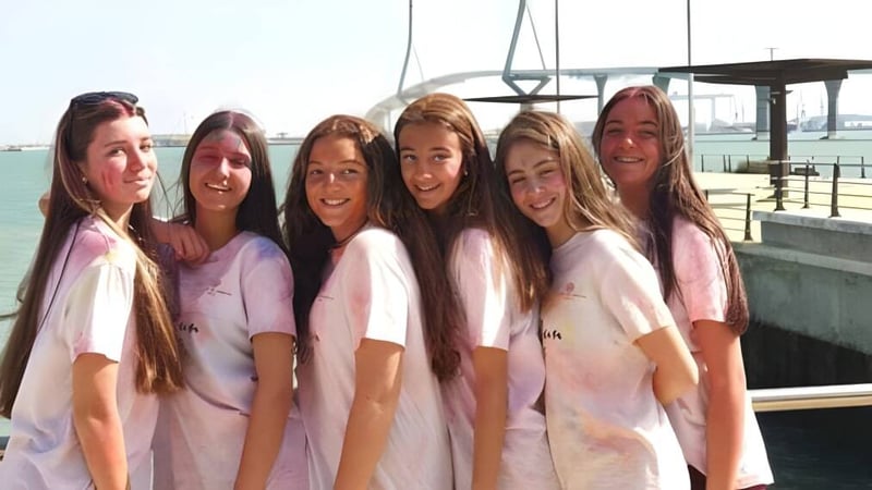 Eine Schülergruppe der San Vicente de Paul School steht in einheitlichen rosa-weißen Shirts vor einem Gewässer mit sichtbarer Brücke.