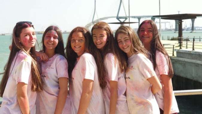 Sechs Schülerinnen der San Vicente de Paul School stehen zusammen vor einem Gewässer mit einer Brücke im Hintergrund.