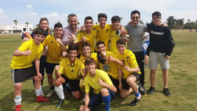 Eine Gruppe von Schülern der San Vicente de Paul School in gelben und blauen Sportuniformen posiert auf einem Rasenfeld mit Palmen im Hintergrund.