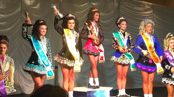 Schülerinnen des Sancta Maria College Ballyroan stehen in farbenfrohen Kostümen auf der Bühne mit Vorhängen und Dekoration im Hintergrund.