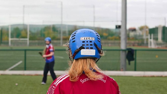 Eine junge Fußballspielerin trägt auf dem Spielfeld des Sancta Maria College (Ballyroan) einen blauen Helm und ein rotes Trikot.