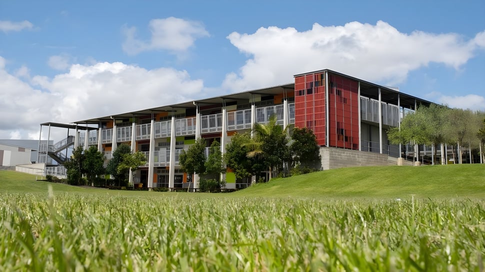 Das moderne Gebäude des Sancta Maria College mit Glas- und Metallfassade steht auf einem grasbewachsenen Feld unter einem bewölkten Himmel.