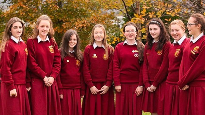 Eine Gruppe Schülerinnen des Sancta Maria College in roten Schuluniformen steht vor herbstlich gefärbten Bäumen.