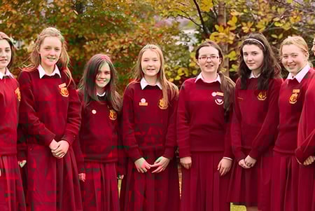 Eine Gruppe von Schülerinnen und Schülern des Sancta Maria College in roten Schuluniformen steht im herbstlichen Gelände mit buntem Laub.
