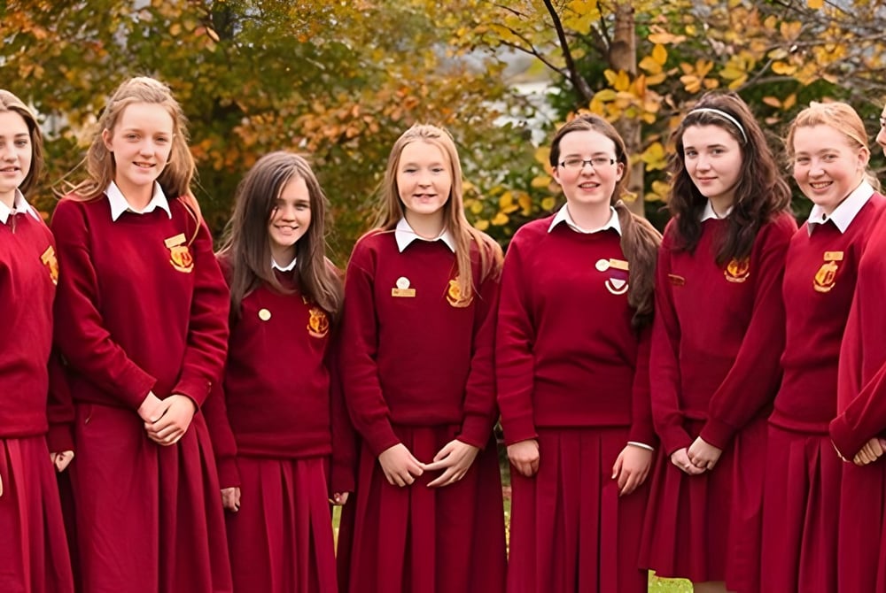 Eine Gruppe von Schülerinnen und Schülern des Sancta Maria College in roten Schuluniformen steht im herbstlichen Gelände mit buntem Laub.